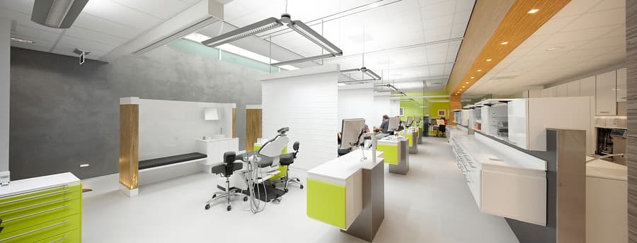 Binnenkant van een orthodontiepraktijk met groene bekleding, behandelstoel en tandartsapparatuur in een lichte, schone ruimte.